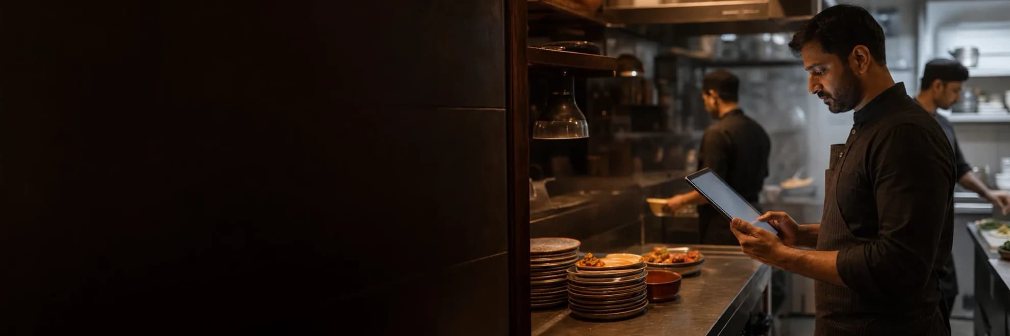 Restaurant kitchen operator reviewing the live shift on a tablet beside the service pass.